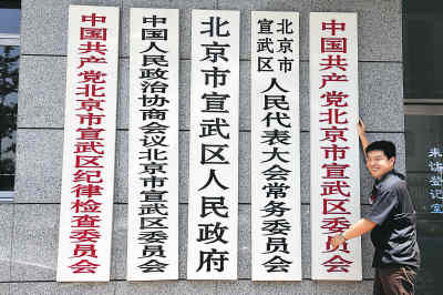7月2日,一位在北京宣武区政府工作的工作人员在即将摘换的宣武区政府机关牌子前留影。江心 摄 7月2日,一位在北京宣武区政府工作的工作人员在即将摘换的宣武区政府机关牌子前留影。江心 摄