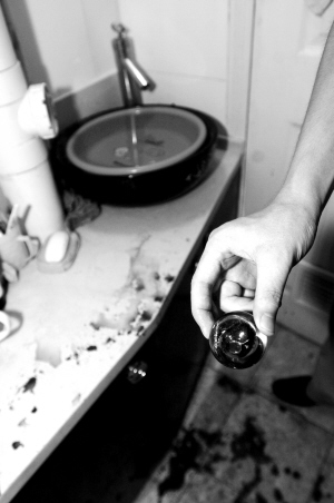 伤者郭女士的丈夫手拿着破裂的水晶龙头,水池边和地面上的血迹仍然