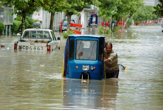 图文:男子推三轮车在被大水淹没的街道前行