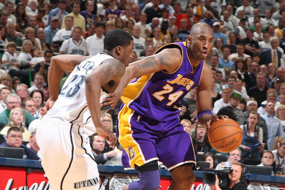 湖人主帅哈姆在场边鼓掌激励队员，背景是斯台普斯球馆的狂热球迷