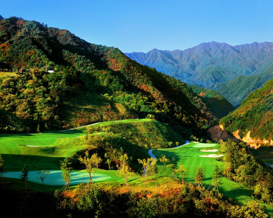晨雾弥漫的山地球场全景，球道如翡翠丝带缠绕在苍翠山脊之间