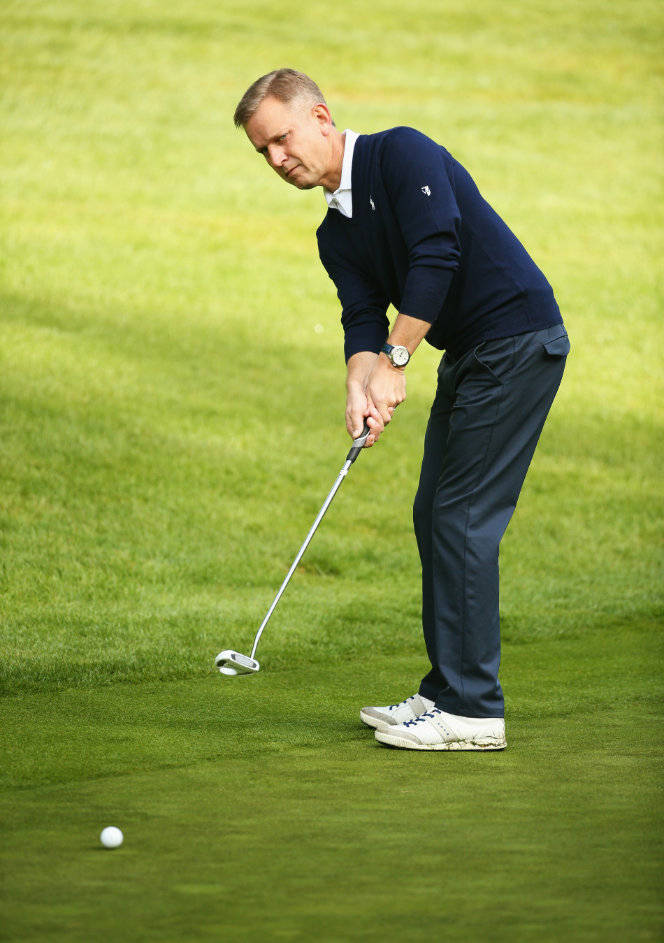 传奇足球明星格伦·霍德尔在球道上专注凝视，与搭档‘白老虎’李·维斯特伍德商讨进攻果岭的策略，阳光将他们思考的身影拉长。