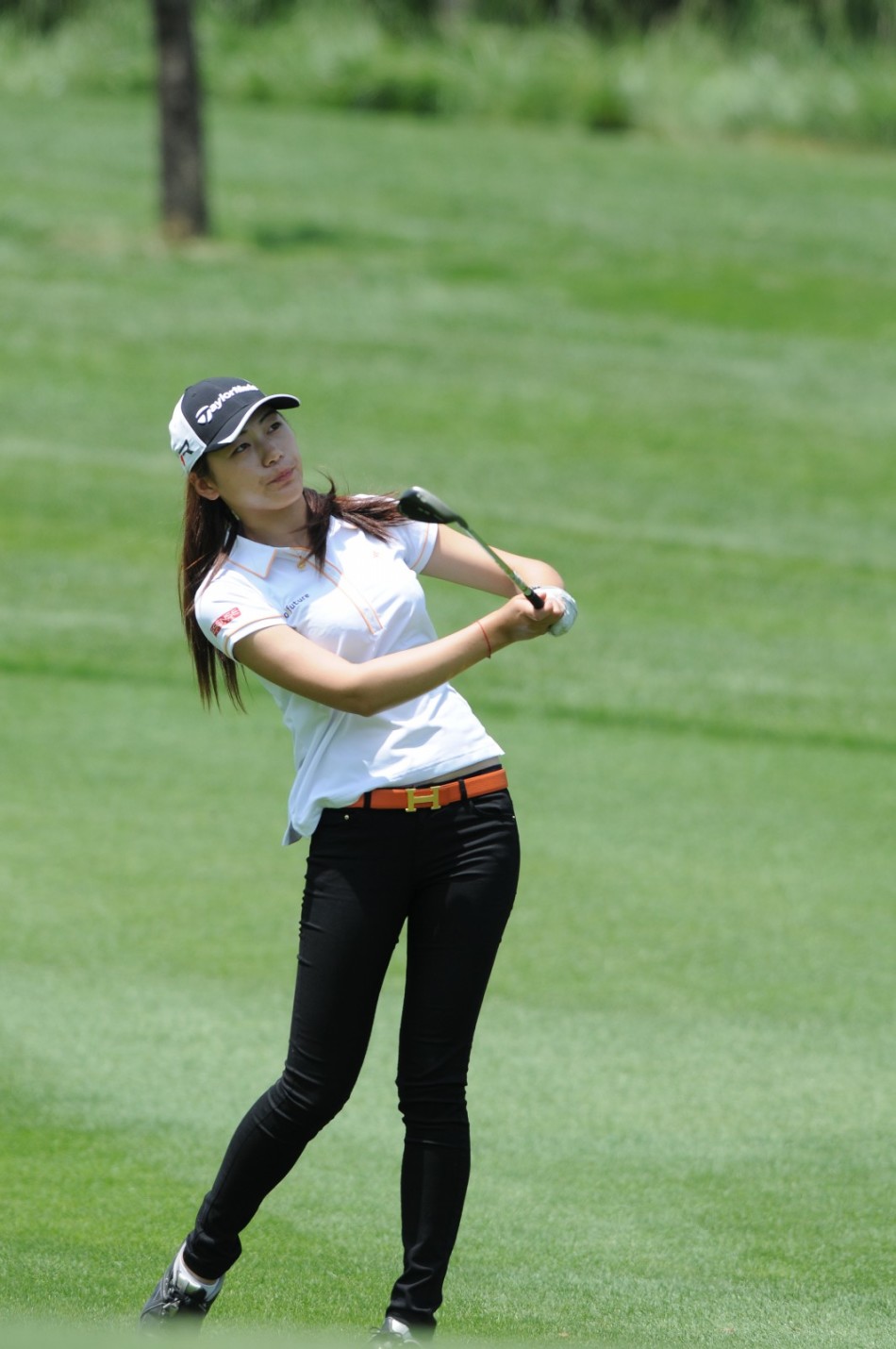 球道之上，女球手潇洒挥杆击球，动作完整而充满力量，阳光勾勒出挺拔身影