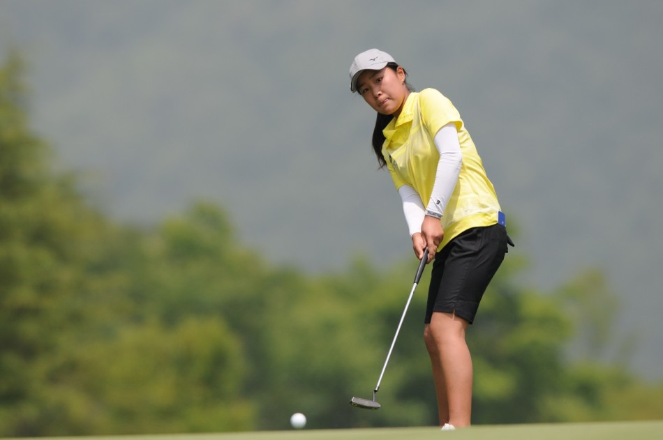 果岭上，球员细心观察推杆线路，神情专注，与身后广阔球场构成和谐画面