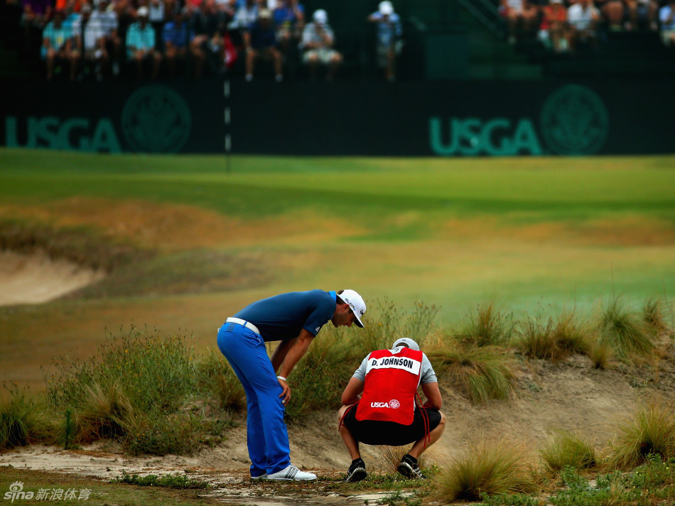 球员从极陡的果岭沙坑沿侧身挥杆，身体保持惊人的平衡，沙粒即将飞扬而起