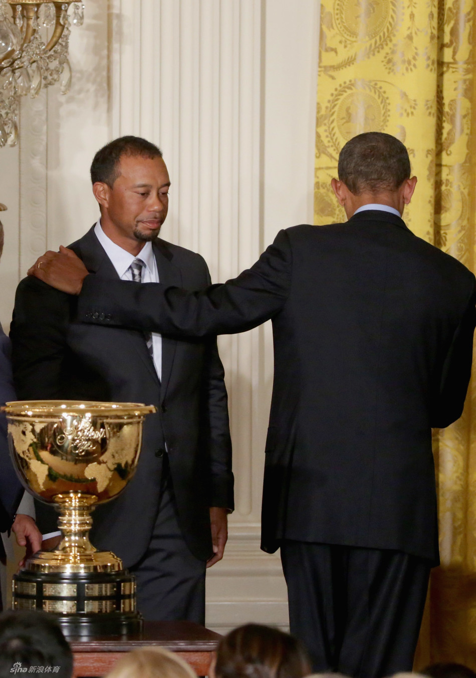 总统讲台侧方，老虎伍兹与扎克·约翰逊并肩站立，伍兹面容沉静，目光专注地望向讲话方向，约翰逊则面带微笑