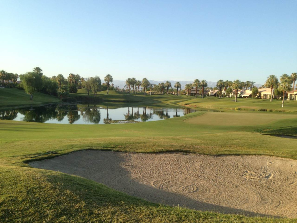 球手从白色沙坑中凝视前方的果岭，沙坑边缘的线条与远方的旗杆构成一幅充满挑战的几何画卷