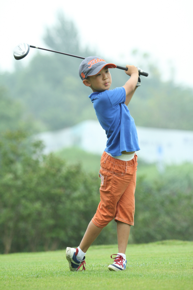 一对父子球员正在果岭边亲切交流，父亲手指远方讲解路线，儿子侧耳倾听，画面充满温情与传承之意。