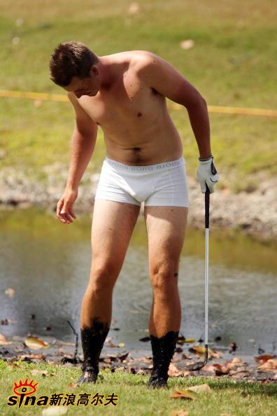 杰森·戴伊站在溪流边的长草中，裤腿高卷，正观察球位，他光着双脚，准备进行一次艰难的救球。