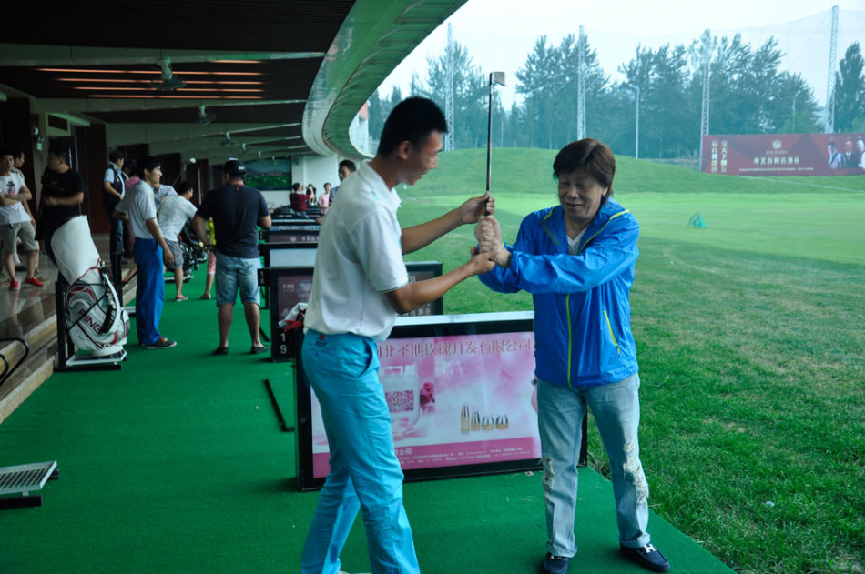 梁小龙在高尔夫练习场认真聆听教练指导,眼神专注如当年研习拳法