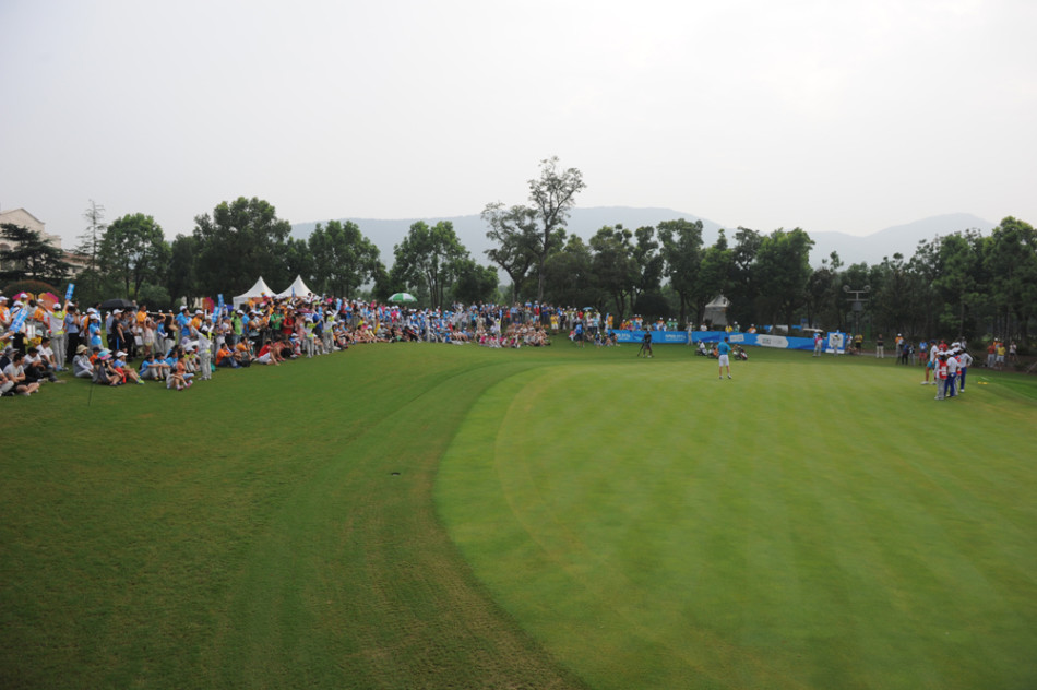 赛场边的亲切交流：巴赫先生与身着各色服装的志愿者们在赛场边围聚，轻松谈笑，气氛融洽，宛如一位长辈在与晚辈们分享见闻。