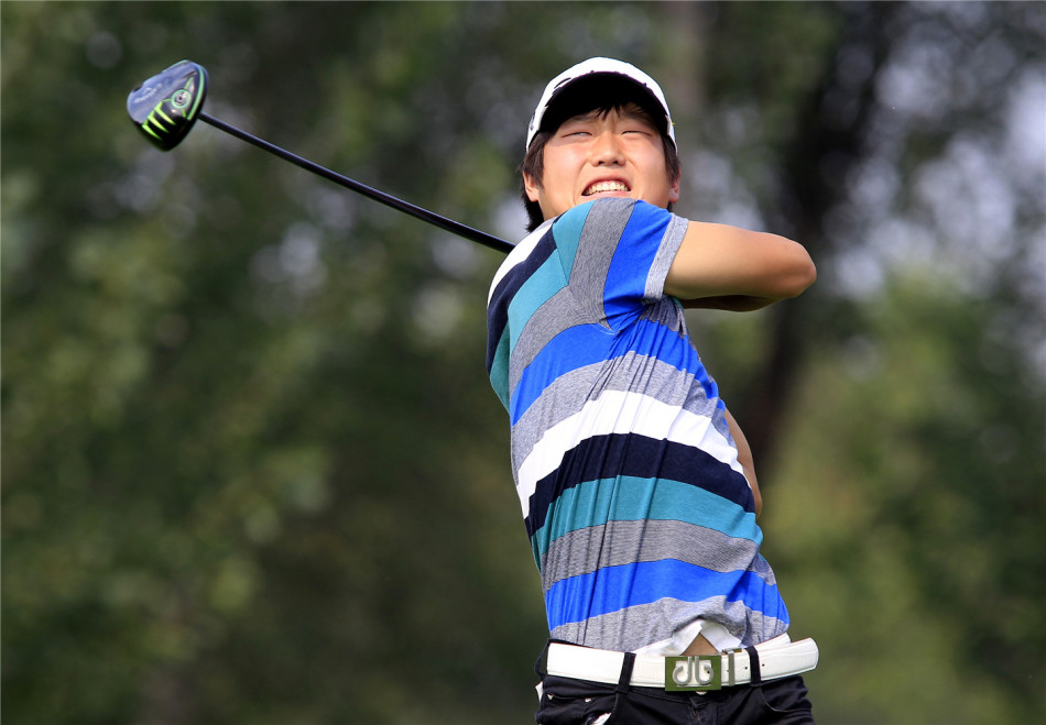 一位女性高尔夫球手在发球台上准备开球，动作标准而充满力量，背景是开阔的比赛场地