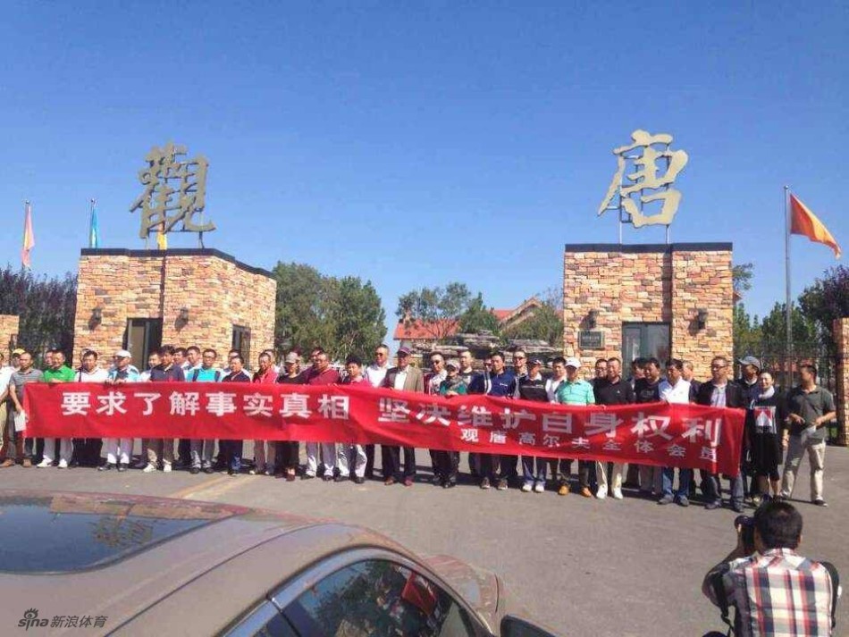 一名身着高尔夫运动装的中年会员正指着远处正在作业的黄色挖掘机，向身旁的同伴激动地诉说着，他们的身后是其他聚集的维权者。