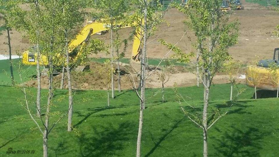 从稍远距离拍摄的现场全景，维权人群与远处多台正在繁忙施工的重型工程机械同框，形成鲜明而讽刺的对比。