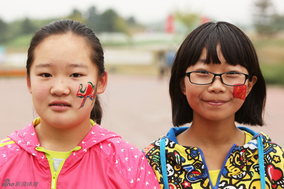 两位年轻女孩开心地对着镜头微笑，她们的脸颊上分别画着创意彩绘，与精心修饰的指甲色彩完美搭配