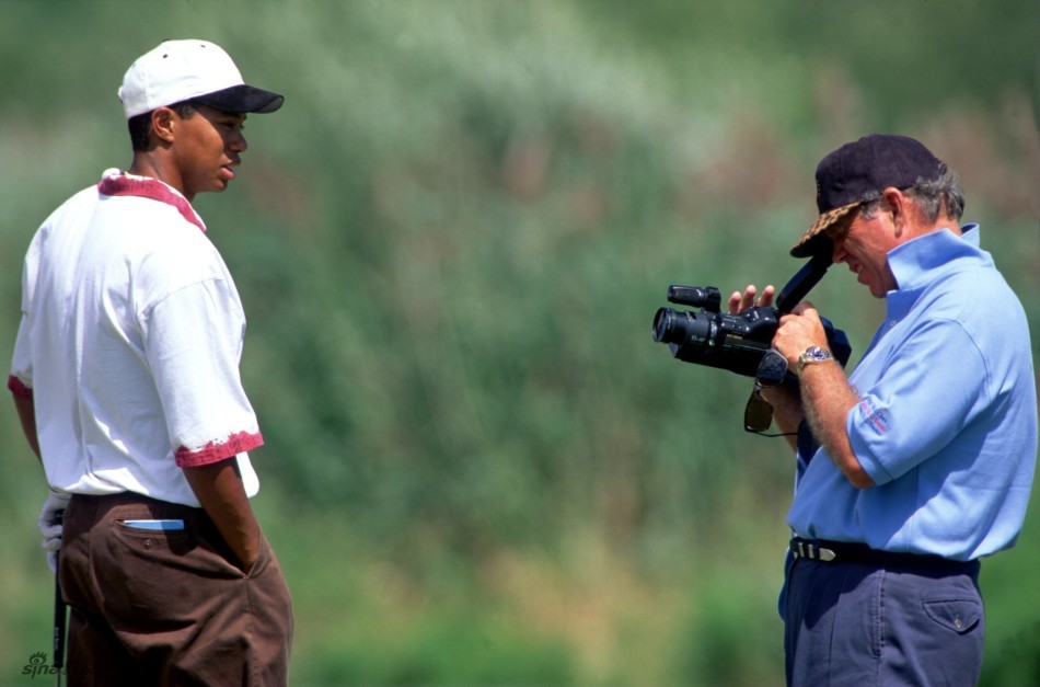 年轻的泰格·伍兹在练习场全神贯注地进行击球训练，目光锐利，动作充满力量。
