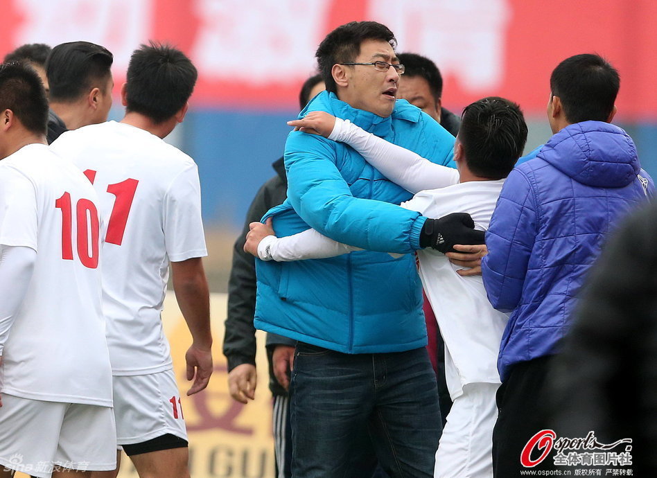 愤怒的白色球衣球员冲破阻拦，紧握双拳直冲向边裁，边裁惊慌躲避，场面混乱一触即发