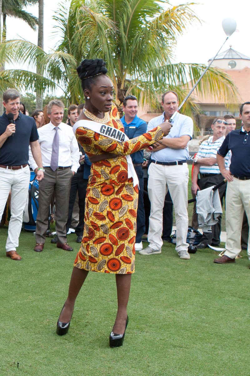 一位金发环球小姐在高尔夫球场练习果岭边，优雅地俯身放置高尔夫球，神情专注。