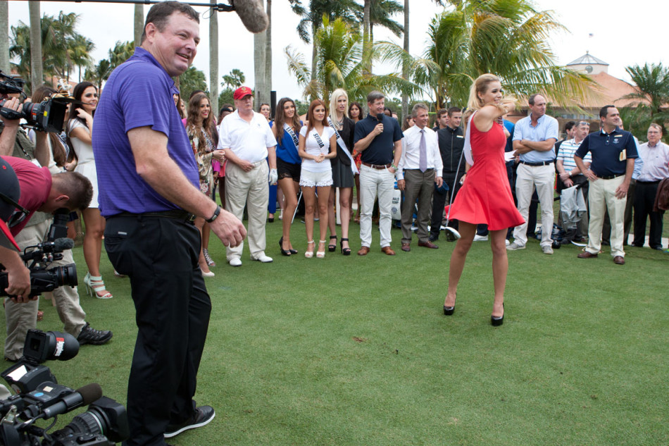 一位佳丽在球场边的树荫下，手持高尔夫球杆露出迷人微笑，阳光透过树叶洒下斑驳光点。