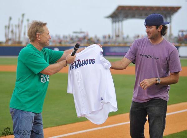 巴巴·沃森笑容满面地接受棒球队赠予的定制T恤衫，展现其作为球队老板与粉丝的亲和一面。