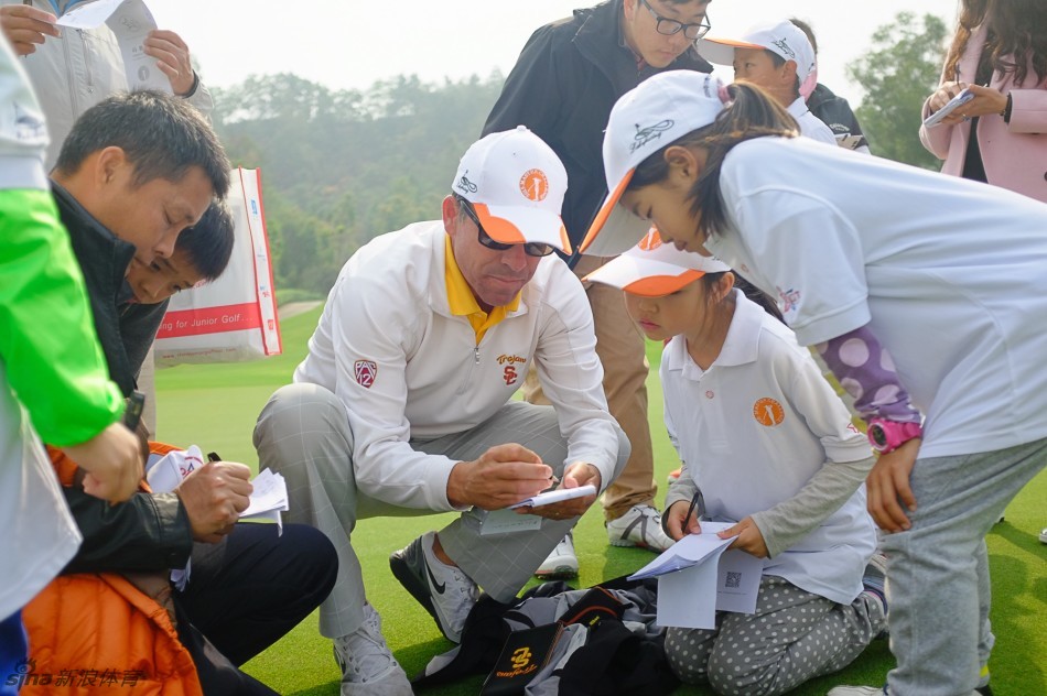 美国教练半蹲在地，手持码数本，正向围坐的选手们生动讲解球场攻略要点