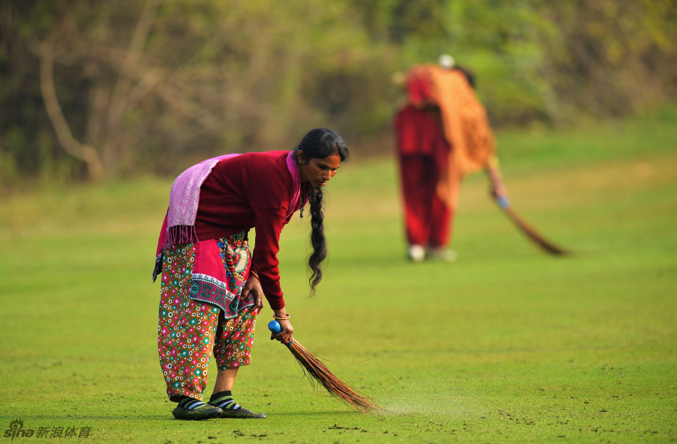 几位身穿鲜艳桃红色与宝蓝色传统纱丽的印度大妈,在高尔夫球场的绿地上并肩行走,笑容灿烂