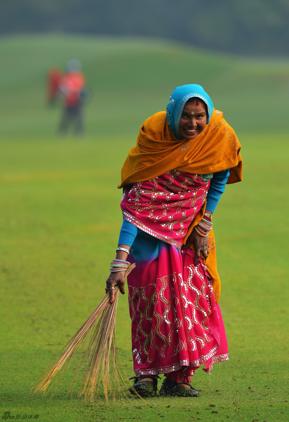 身穿传统服饰的印度大妈手持扫帚,在清晨的球场树荫下认真清扫落叶,画面宁静而充满生活气息