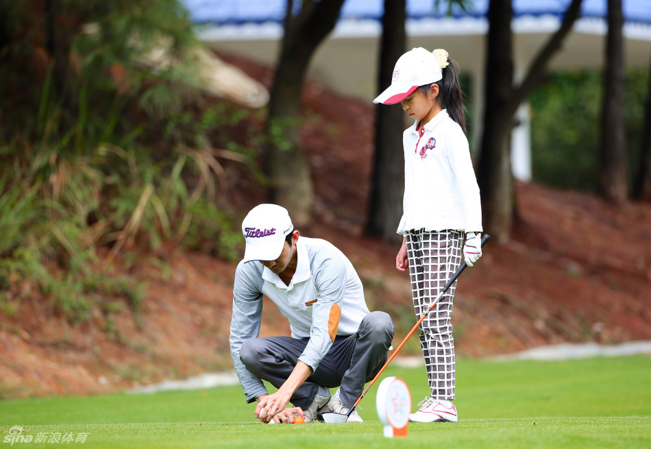 小选手在果岭上小心地将旗杆插回洞杯，动作一丝不苟，脸上带着完成挑战后的满足感，'插这么高刚刚好'的专注神情令人动容。