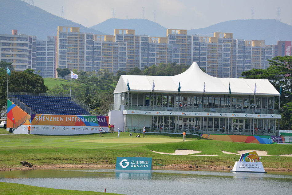 两位女球迷站在第十八洞果岭旁，聚精会神地观看比赛，脸上洋溢着对运动的热爱。