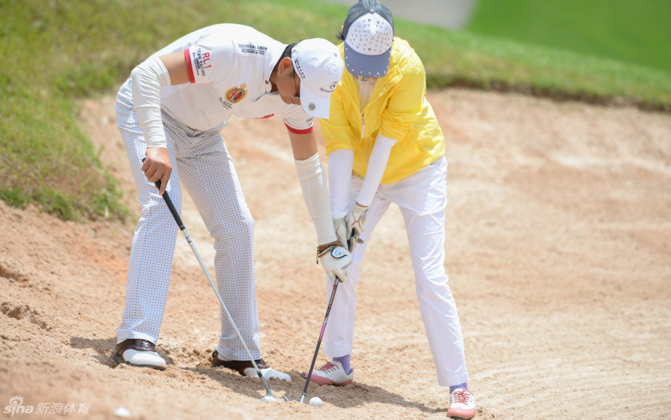 队友在沙坑中互相帮助，一位球员正俯身指导同伴如何救球，完美诠释了团队协作的体育精神。