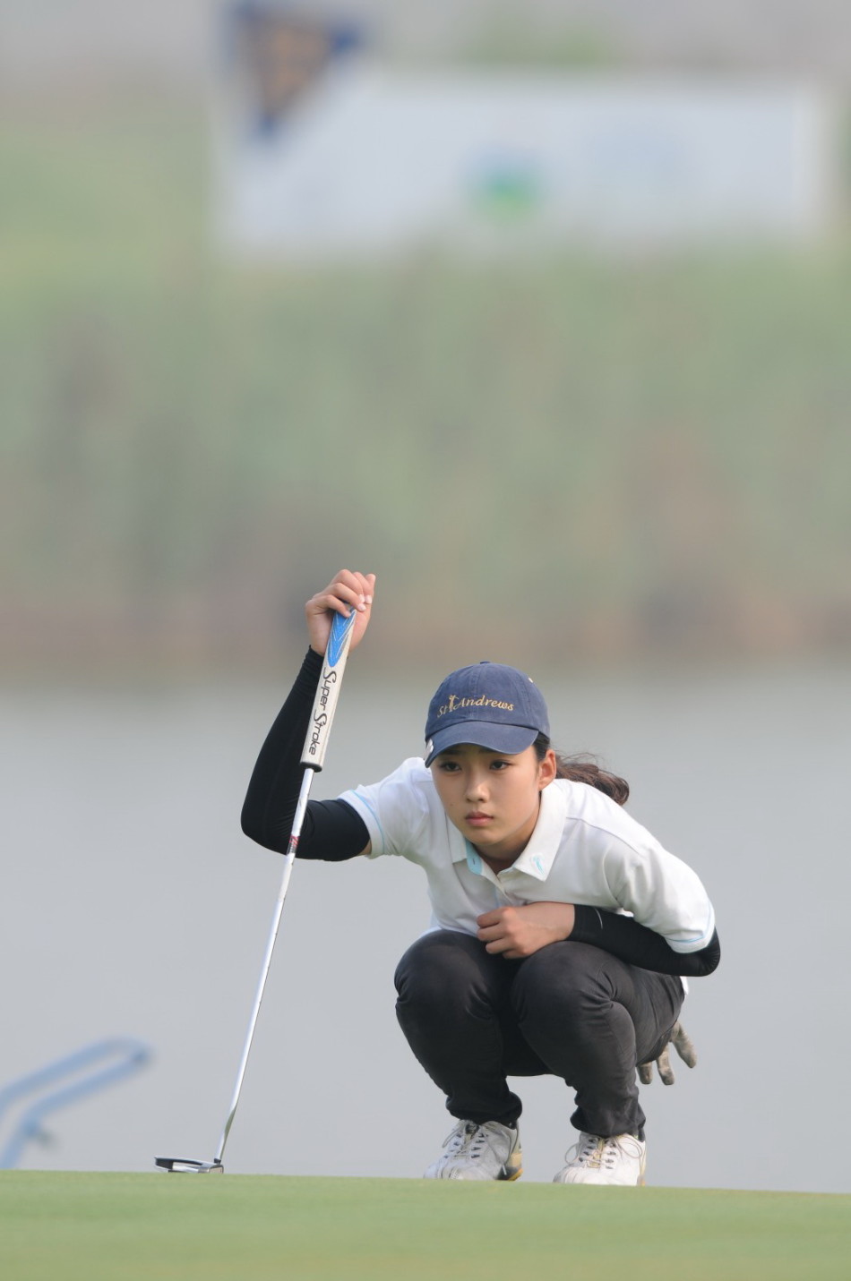 刘思芸在发球台或球道上扬起一把草屑测试风向，她的动作自然专注，体现了球员利用一切自然信息做出决策的专业素养。
