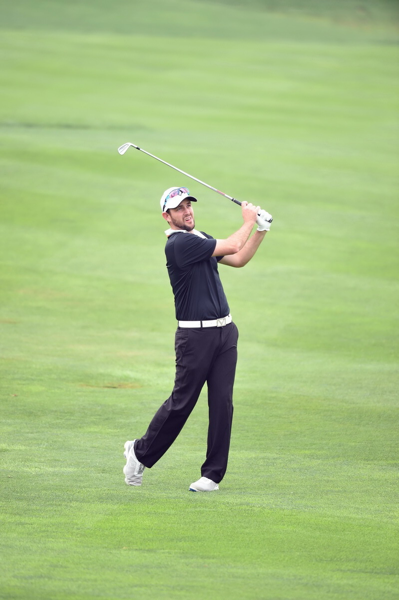 高尔夫选手Nathan Stubbs在开阔的球道上全力挥杆，球杆划出完美弧线，小球向远方果岭飞去。