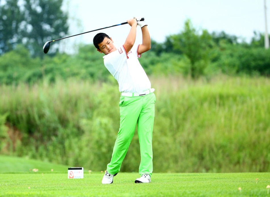 一位小球员手持推杆，正在果岭上仔细观察推击线路，神情沉着冷静，仿佛一位久经沙场的老将。