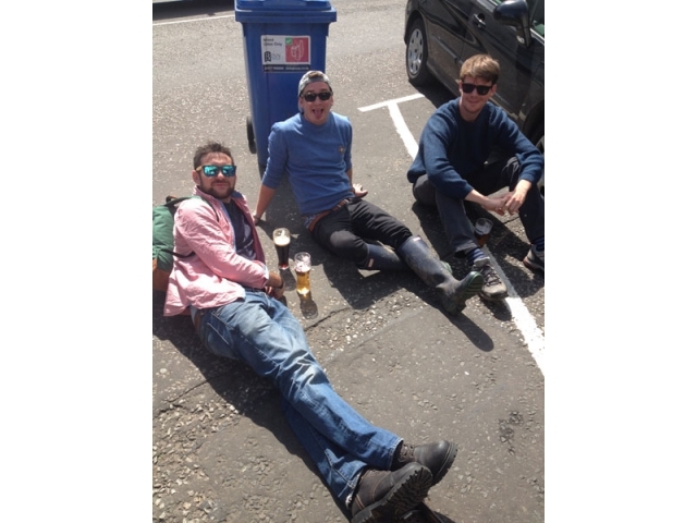 酒吧内景，木质吧台后酒柜上摆满了各式威士忌，暖黄的灯光下人们簇拥在一起，氛围热烈而融洽，墙上隐约可见密密麻麻的纪念相框。