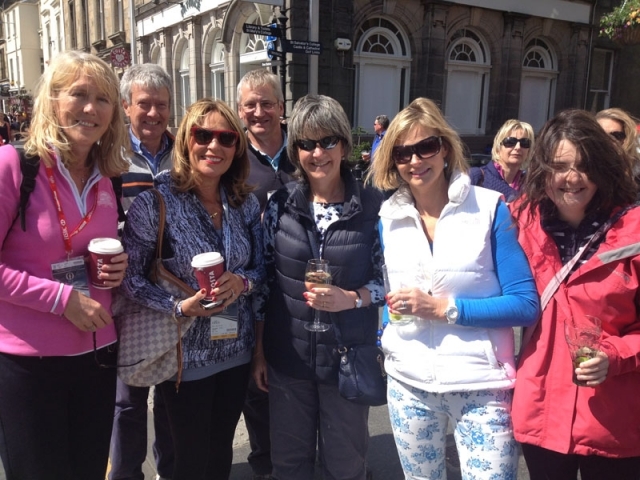 一位身穿亮黄色雨衣的女士在露天餐区仰头大笑，手中紧握着一杯金色的啤酒，尽管天气阴郁，她的笑容却极具感染力。