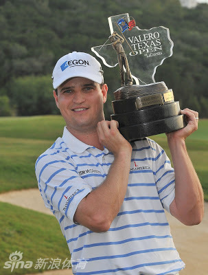 扎克·约翰逊在美国大师赛胜利后，深情注视手中的冠军奖杯，绿夹克的荣耀在肩头闪耀