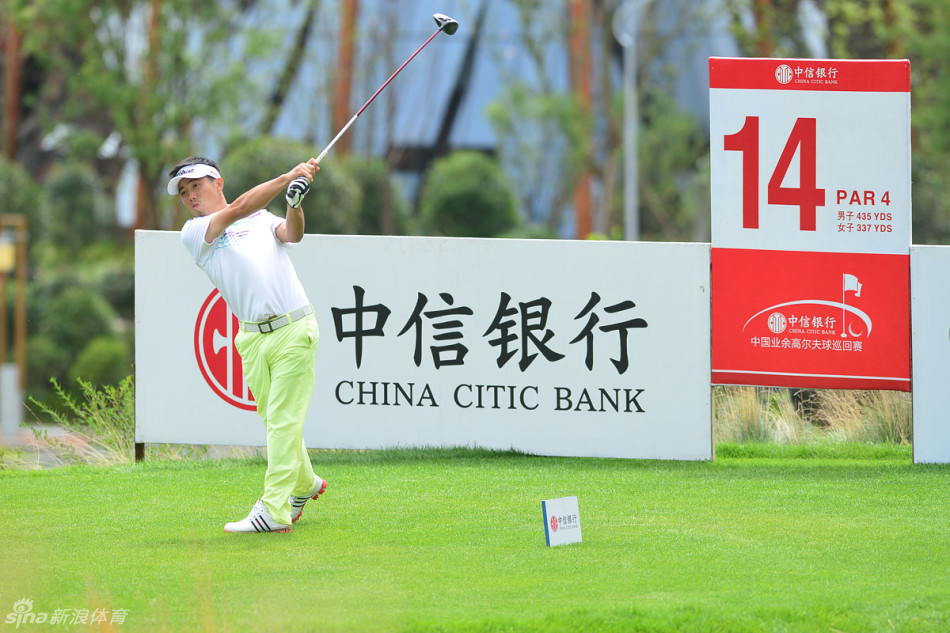 球手陈敏柔在第十四洞的发球台上侧身测风，衣裙与发丝随风轻扬，眼神专注地判断着风向与力度，为关键一击做准备。