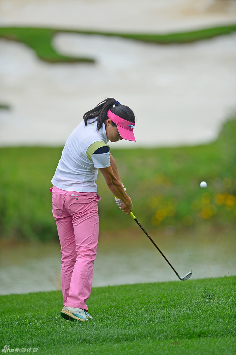 一位身着红色上衣的球手正专注地在沙坑中救球，沙坑边缘的白色与那抹亮红形成鲜明对比，展现了困境中的沉着与技巧。