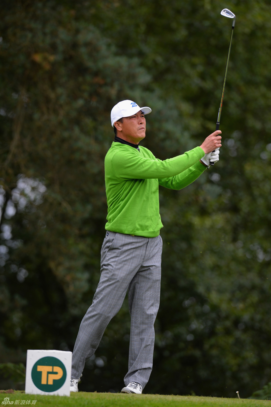 张连伟手扶球帽，目光如炬地凝视远方球道，帽檐下的眼神透露出精准计算的专注