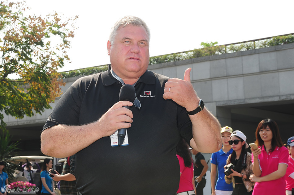 中国职业球员张新军与一位业余搭档并肩走在球道上,两人面带笑容轻松交流,完美体现了配对赛的友谊精神。