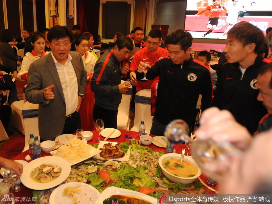 辽足功勋主帅马林与老将王亮在铁西体育场外俯身微笑，耐心地为满脸稚气的小球迷在球衣上签名，画面充满了温情与传承的力量。