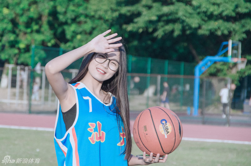 任丹妮轻撩起被风吹乱的秀发，背景是汕头大学的篮球架与黄昏的柔光，整个画面充满了动态的青春美感。