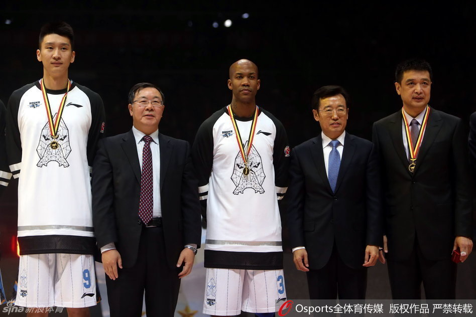 比赛暂停间隙，北京队主教练闵鹿蕾手持战术板，神情严肃地为队员们布置战术，他的身后是刚刚升起的总冠军旗帜，此刻球队正面临严峻考验。