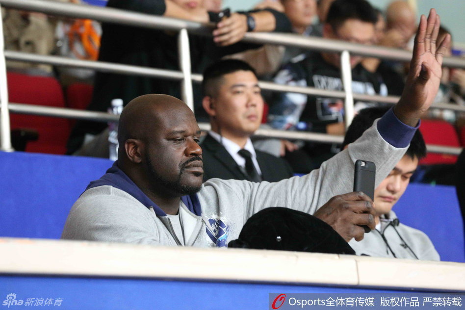 奥尼尔调皮地拿起手机对准姚明拍照，而姚明则面带微笑地看向镜头，两人之间的互动充满了老友重逢的趣味与温馨。