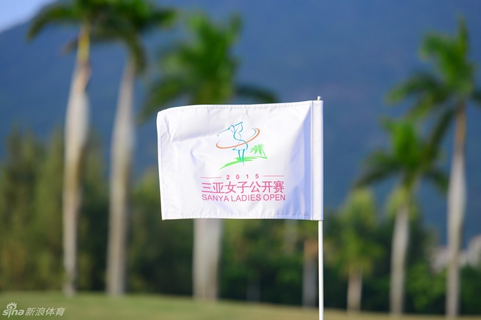 从高处俯瞰亚龙湾球场全景，碧绿的球道如丝带般在椰林与沙坑间蜿蜒，尽头是浩瀚的蔚蓝大海，构成一幅充满热带风情的壮丽图画。