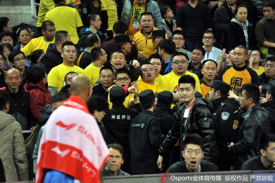 混乱之中，一名身着深色外套的球迷试图冲破安保人员的阻拦，他的身体前倾，手臂用力地向前伸，而在他面前，一名年轻的安保人员正全力阻挡，表情坚毅而吃力。