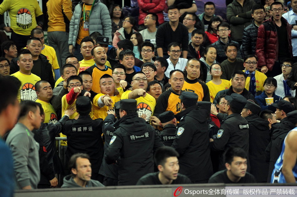 混乱的看台通道内，几名安保人员手挽手形成一道警戒线，努力将情绪激动的球迷隔离开来，为身后的裁判组开辟出一条狭窄而艰难的撤离通道。