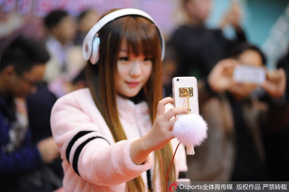 这位身材惹眼的女球迷在场边安静地观看比赛，侧面轮廓优美，她手中拿着助威棒，背景是激烈的赛场对抗。