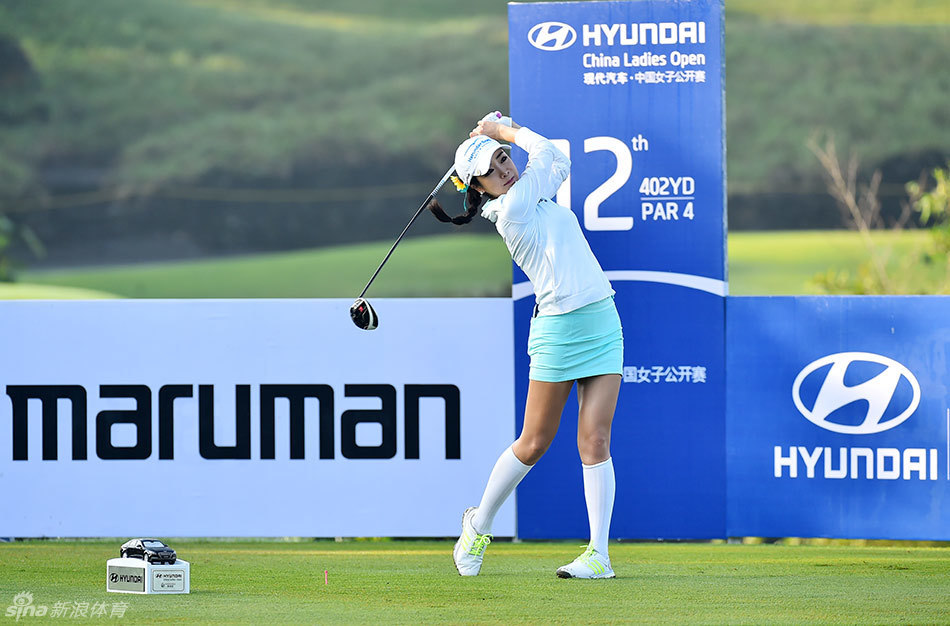 韩国选手安信爱在球道上露出标志性的开朗笑容，阳光洒在她的面庞与身后的赛事背景板上，显得自信而从容。