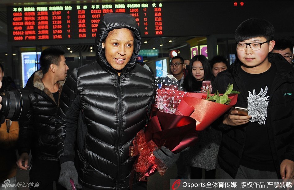 热情的山西女球迷手捧精美的鲜花，在人群中踮起脚尖，急切地将花束递到玛雅·摩尔面前，表达对她的喜爱。